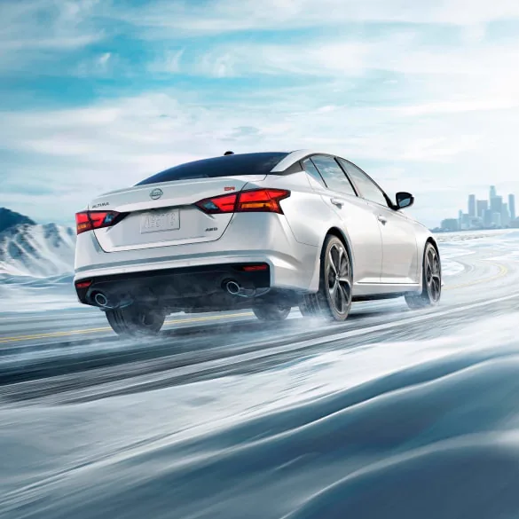 2027 Nissan Altima in white seen from behind driving in snowy landscape illustrating all-wheel drive at Holler Nissan Columbia in Columbia SC